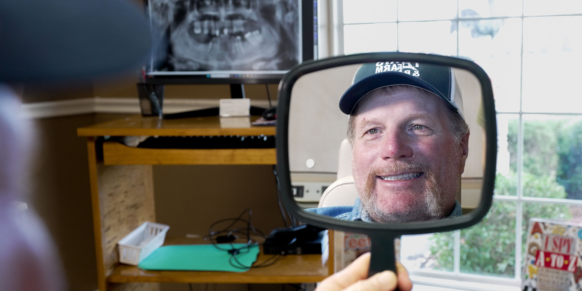 man with hat new teeth looking in mirror